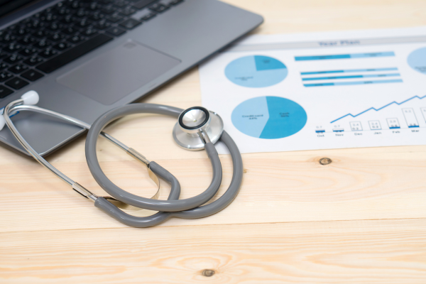 A laptop, stethoscope and paper with charts to imply accounting in healthcare